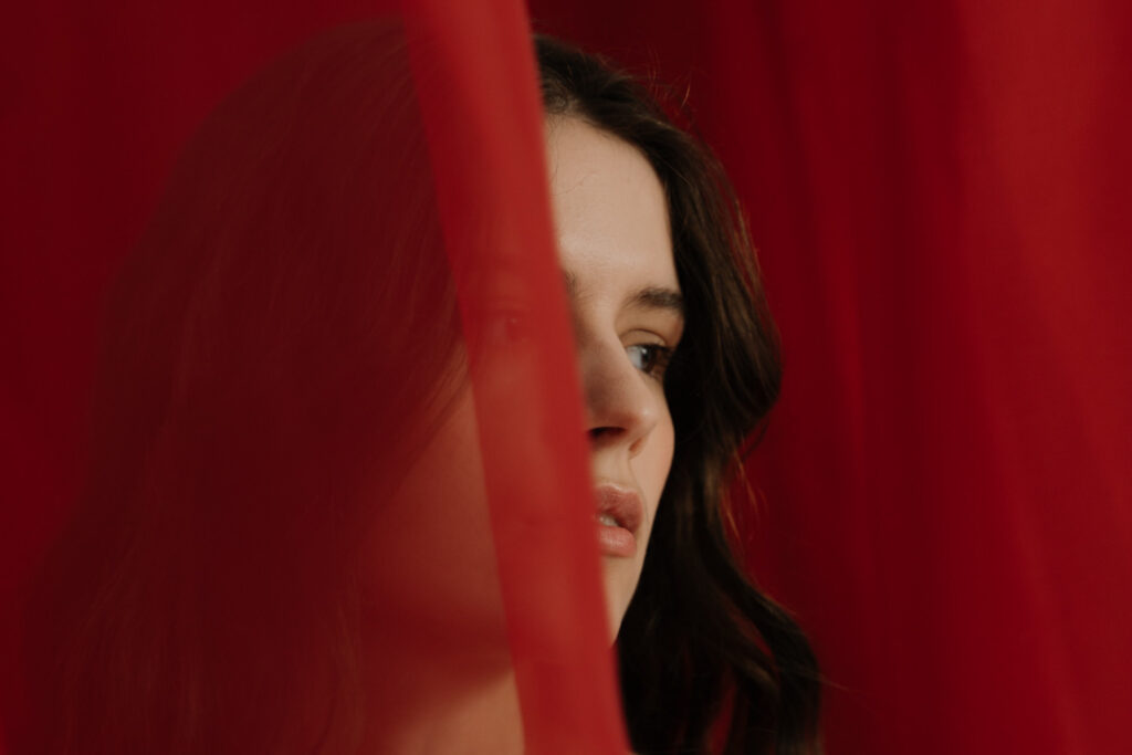 close up of a woman hiding in a red transparent cloth