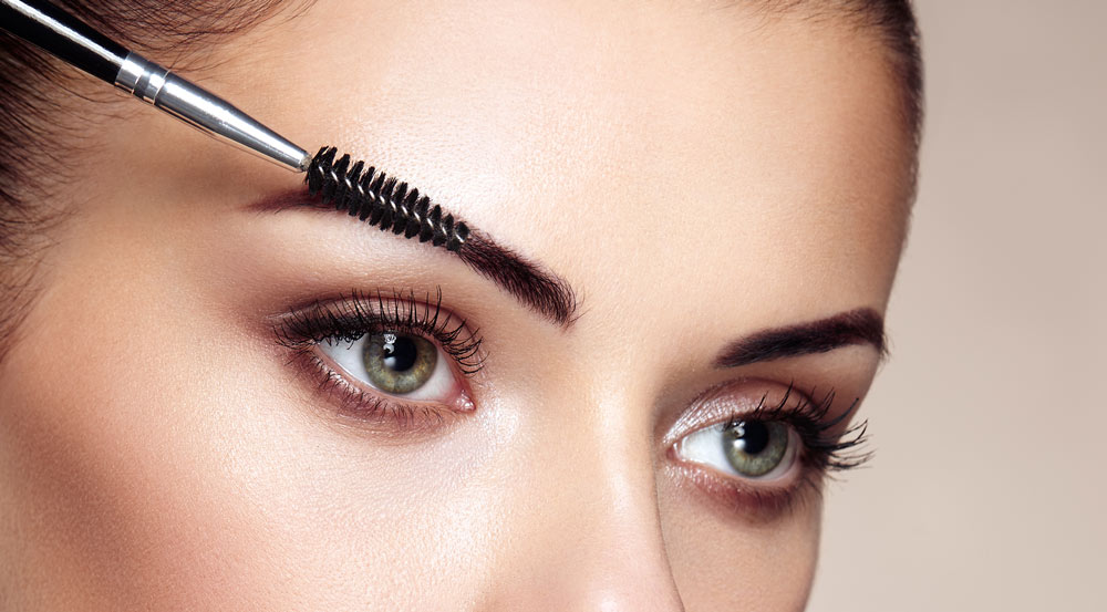photo of a womans green eyes while shaping eyebrows with an eyebrow brush