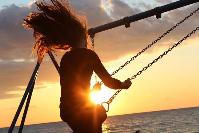 woman swinging on swing with sunset on the beach in background