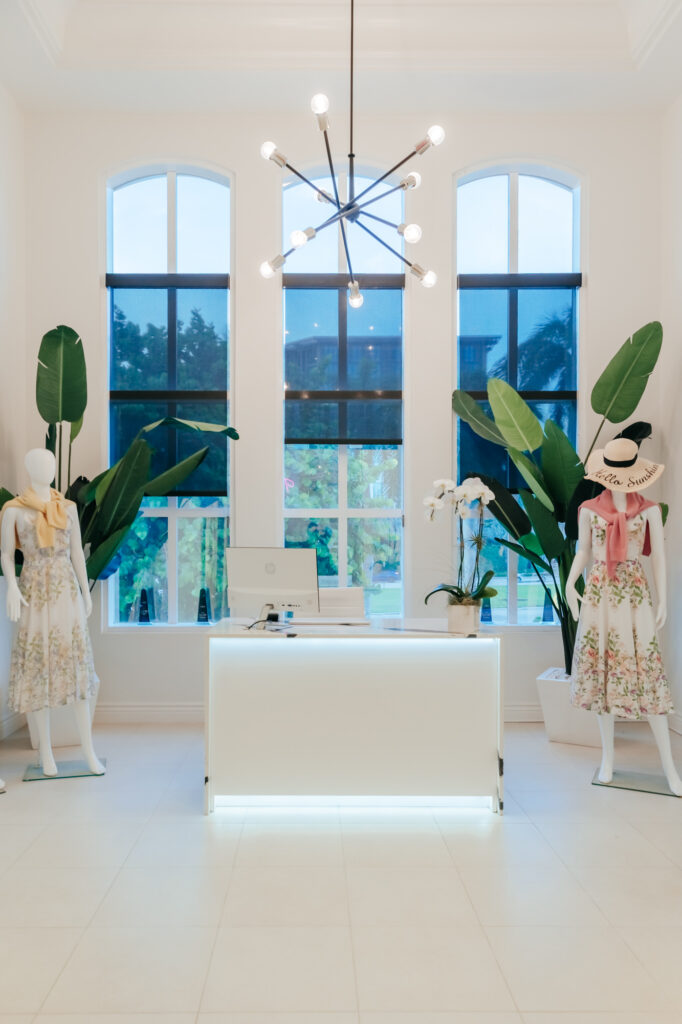 White interior room with female mannequins, two large plants, and three tall windows side by side