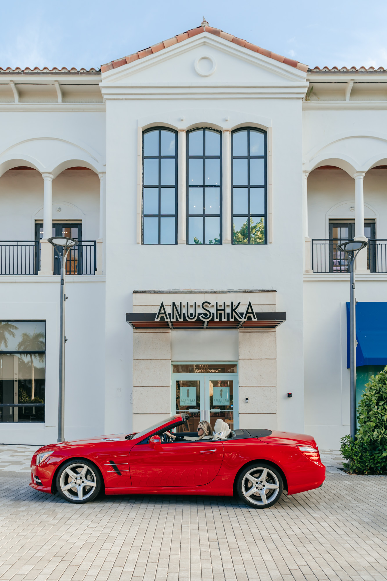Woman driving away from Anushka Spa Salon in a red convertible