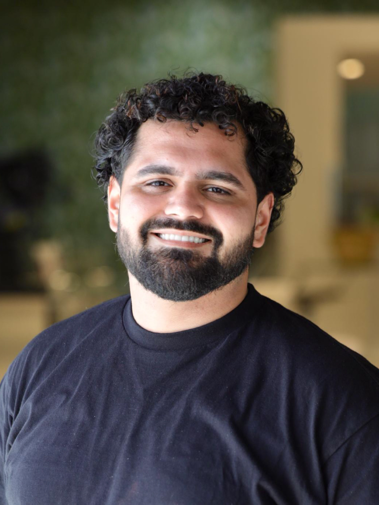 Portrait of Lucho; a man with black, curly hair, short beard, and a black shirt