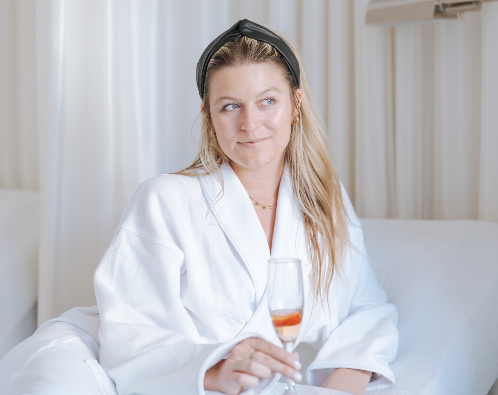 A young woman wears the luxurious Anushka robe while enjoying an infused water. She's ready for her Brazilian lymphatic drainage massage in West Palm Beach.