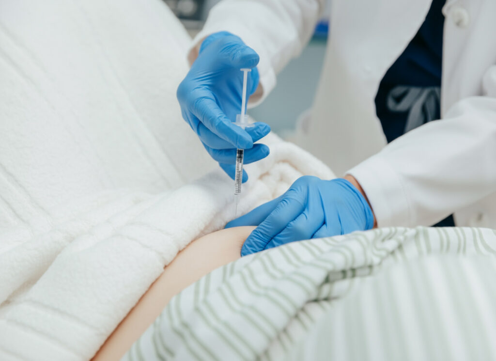 A physician gives a woman a weight loss injection using a hypodermic needle. It is inserted into her stomach as he presses the needle in.