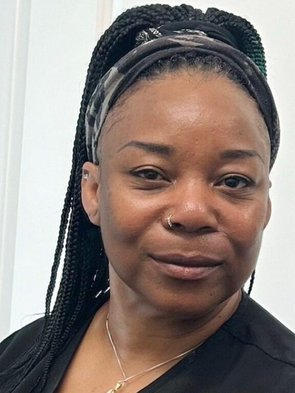 Portrait of Barbara, a smiling woman with long black hair in braids with a headband wearing a black massage uniform.