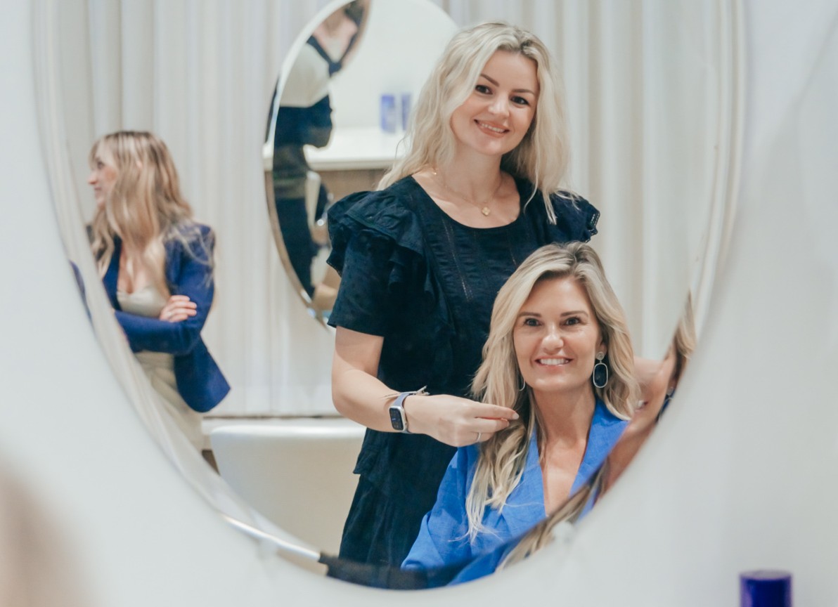 A senior stylist and a female client look in a mirror, talking through what the client wants to do before her haircut in West Palm Beach.